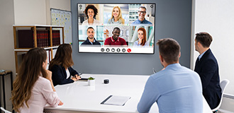people sitting at a table in a conference room looking at a video conference screen
