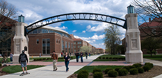 Arched purdue university sign at the entrance to the university, with students walking and campus buildings in the background
