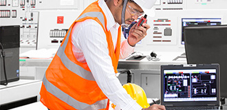 worker in hard hat and safety vest talks on a radio inside a control center