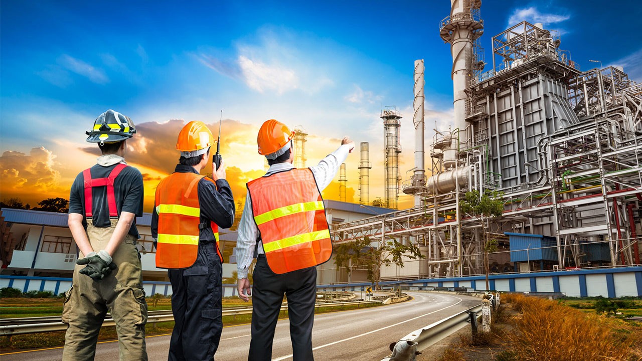 Three construction workers looking at a refinery